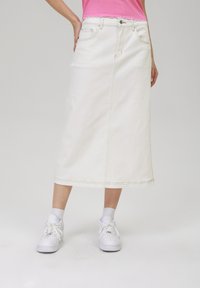 Jupe midi en denim blanc avec poches avant et arrière, couture visible et coupe droite. Associée à des baskets blanches et des chaussettes grises.