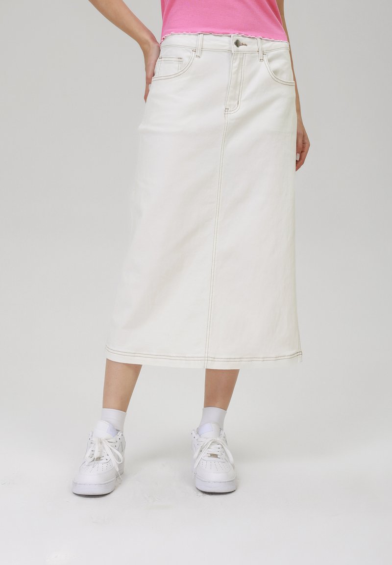 Jupe midi en denim blanc avec poches avant et arrière, couture visible et coupe droite. Associée à des baskets blanches et des chaussettes grises.