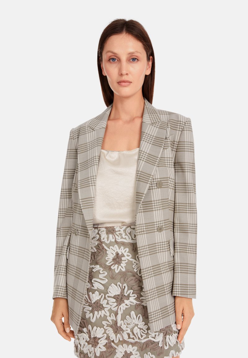 Grau karierter, doppelt geknöpfter Blazer mit strukturiertem Design, mit Reverskragen und Vordertaschen, getragen über einem cremefarbenen Oberteil und einem gemusterten Rock.