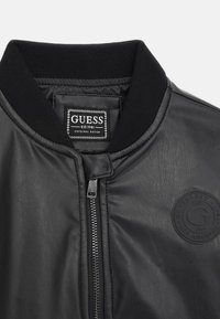 Giacca bomber nera in pelle con colletto a coste, chiusura con zip e patch con logo in rilievo. Texture liscia con dettagli di cucitura minimi.