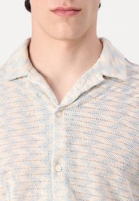 Camisa de manga corta en azul claro y crema, con un patrón texturizado de zigzag, cierre de botones y una tela suave y transpirable.