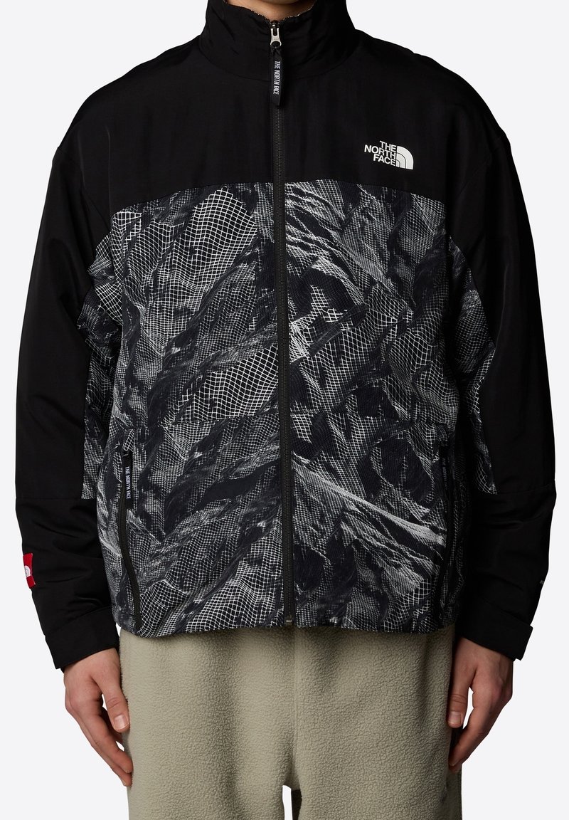 Svart zip-up jacka med ett grafiskt mönster i nyanser av grått, med hög krage och kontrasterande ärmdetaljer. Texturerad tyg.