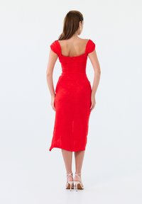 Robe midi rouge ajustée avec des manches bouffantes, décolleté carré et fermeture éclair au dos. Tissu lisse avec un motif subtil. Silhouette élégante.