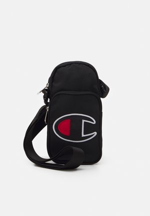 Schwarze Umhängetasche mit verstellbarem Trageriemen, mit großem rot-weißem Champion-Logo auf der Vorderseite, vor einfarbigem Hintergrund.
