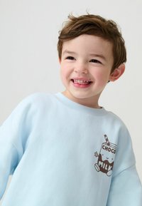 Svijetloplava dukserica od mekanog materijala, s smeškom i slamčicom na smešnom smešnom crtanom mlijeku s smeškom na lijevoj strani prsnog dela.