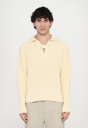 Light yellow ribbed pullover with a collar, button detail, and long sleeves. The fabric has a textured finish and a relaxed fit.