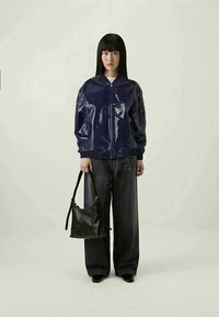 Mornarsko sijoče bombersko jakno z zadrgo spredaj, rebrastimi manšetami in stranskimi žepi, v kombinaciji s širokimi temnimi kavbojkami in majhno črno torbico čez ramena.