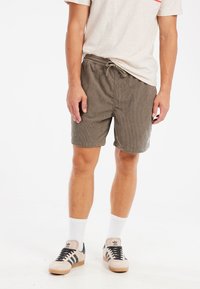 Gråstribede shorts med elastisk talje og justerbar snor. Bærer med hvide ankelstrømper og beige sneakers med sorte accenter.