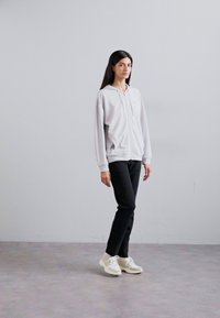Fleece cinzento claro com fecho éclair, com um logotipo subtil, combinado com calças pretas e ténis brancos. O conjunto apresenta um tecido macio e suave.