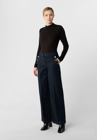 Ciemne dżinsowe spodnie o szerokich nogawkach z złotymi guzikami, frontowymi kieszeniami i prostym krojem. Połączone z dopasowaną czarną bluzką z długim rękawem.