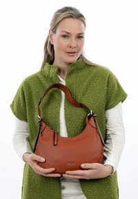 Sac à main en cuir marron avec une forme incurvée, sangle noire contrastante et petite poche zippée ; présenté sur un fond blanc.