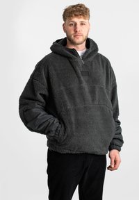 Felpa con cappuccio in pile color grigio scuro, dotata di collo con zip, polsini elasticizzati e una superficie morbida e testurizzata con un filetto di tessuto sul petto.