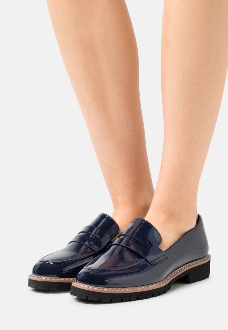 Mocassins en cuir verni bleu marine brillant avec semelles épaisses à crampons, portés pieds nus, vus de face et de côté.