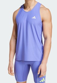 Top da allenamento viola con tessuto testurizzato, caratterizzato da un logo bianco. Indossato con pantaloni corti compressivi viola coordinati e dettagli.