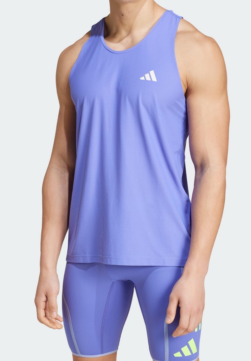 Top da allenamento viola con tessuto testurizzato, caratterizzato da un logo bianco. Indossato con pantaloni corti compressivi viola coordinati e dettagli.