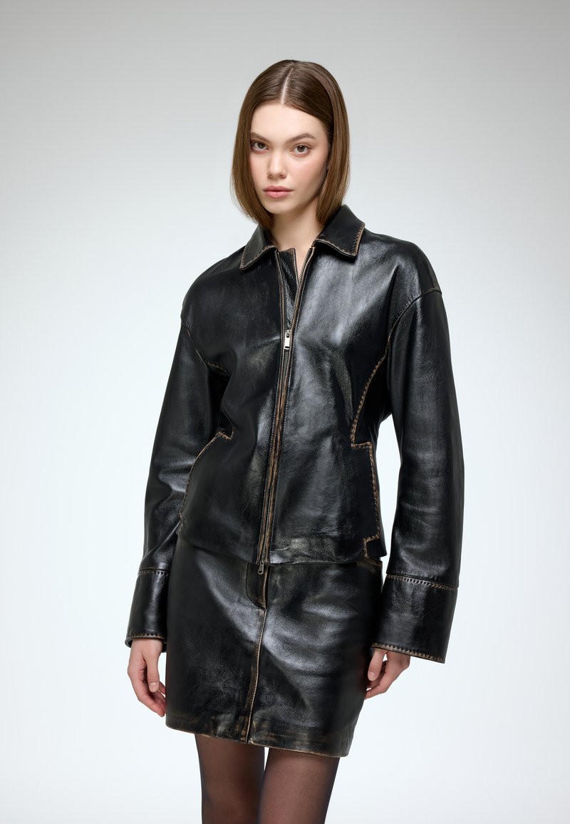 Black leather jacket with a collar and zip closure, featuring contrasting stitching and a fitted design, paired with a matching leather skirt.