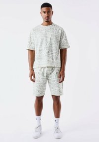 Conjunto de algodón de color verde claro que incluye una camiseta de manga corta y un pantalón corto, ambos con un patrón de texto repetido. Incluye zapatillas blancas y calcetines.