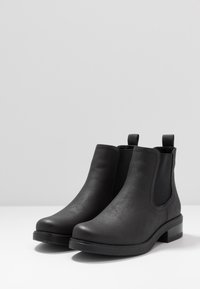 Bottes noires en cuir à hauteur de cheville avec des panneaux latéraux élastiques, bout rond, petit talon bloc et anses pour un enfilage facile. Texture lisse et design minimaliste.