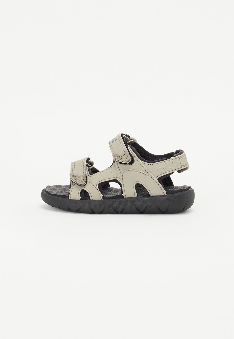 Sandale beige pour enfant à bout ouvert avec semelle noire et brides en Velcro réglables sur les orteils, la cheville et le talon.