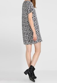 Mustat ja valkoiset kukkakuosiset lyhyet mekko, jossa on rento istuvuus, lyhyet hihat ja pyöreä pääntie, yhdistetty mustiin nilkkasaappaisiin.