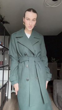 Manteau double boutonnage vert avec une ceinture, larges revers, manches longues et tissu texturé. Doté de boutons noirs et d'une coupe décontractée.