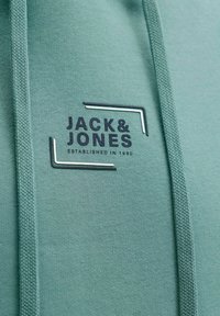 Grüner Hoodie mit strukturierter Stoffqualität, Logo mit "JACK & JONES" in Dunkelblau und minimalistischem Design mit Nahtdetails.