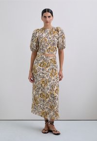 Woman wearing matching animal print puff-sleeve crop top and long skirt, standing with black strappy sandals against a plain background.