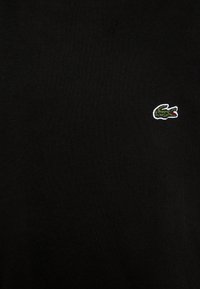 Svart bomull t-shirt med korta ärmar, med en liten grön och vit broderad krokodil-logotyp på vänster bröstområde.