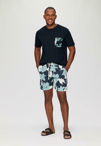 Marine t-shirt met een gemust pocket, gecombineerd met blauwe en witte bloemen shorts. Bruine sandalen maken de casual zomerlook compleet.