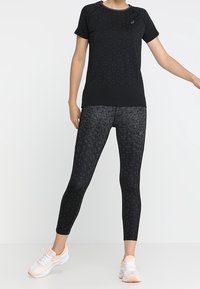 Svart atletisk t-shirt med ett subtilt mönster, i kombination med svarta leggings som har en kontrasterande texturerad design, kompletterat med ljusa sneakers.