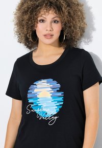 Černé tričko s kulatým grafickým motivem pruhů v modré a žluté barvě, s nápisem "Sunshine Valley" v bílé ruhové písmě pod designem.