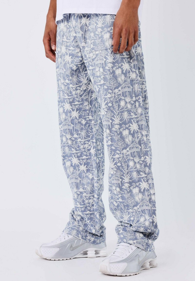 Pantalons bleu clair à motifs tropicaux, avec des palmiers et des huttes blancs. Le tissu est doux, avec une taille élastique et des poches.