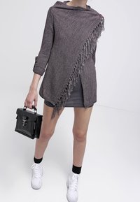 Poncho grigio lavorato a maglia con design asimmetrico, orlo sfrangiato e dettaglio con bottoni. Abbinato a una borsa nera e sneaker bianche.