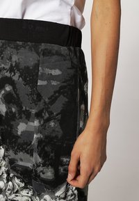 Pantaloni con elastico nero in vita e un motivo astratto grigio e nero, dotati di tasca laterale e tessuto testurizzato.