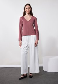 Top rosa empolvado de manga larga con escote en V y detalles de costura, combinado con pantalones anchos blancos y flats negros. Texturas de tela simples y suaves.