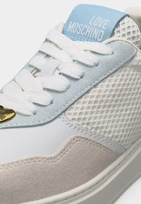 Baskets blanches, beige et bleu clair avec des lacets blancs, des côtés en mesh, un détail en daim et une étiquette "LOVE MOSCHINO" sur la languette.