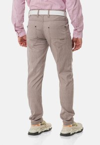 Beige gestreifte Hosen aus strukturiertem Stoff, im niedrigen Schnitt, mit Gesäßtaschen und einem weißen Gürtel, kombiniert mit beigen Sneakern.