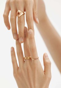 Tres anillos de oro exhibidos en dedos: un anillo texturizado con un corazón, un anillo liso con piedras, y un anillo audaz con un diseño de estrella.