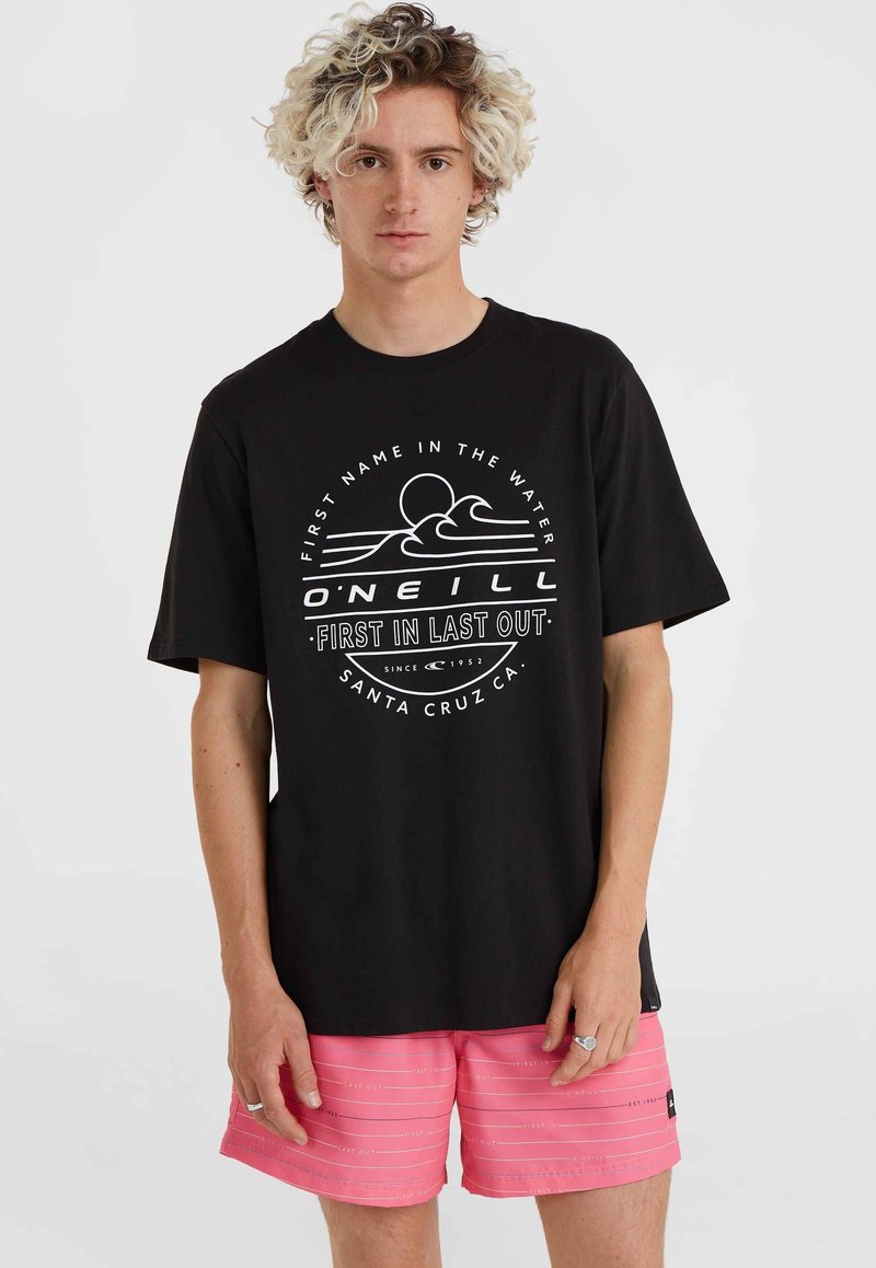 Camiseta de algodón negra con estampado gráfico blanco que presenta olas y un sol, combinada con bañador rosa que muestra rayas blancas horizontales.