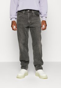 Mörkblekta svarta jeans i denim med rak benform. Har fem fickor, bälteshällor och en silverfärgad knappstängning. Kombinerade med vita sneakers.