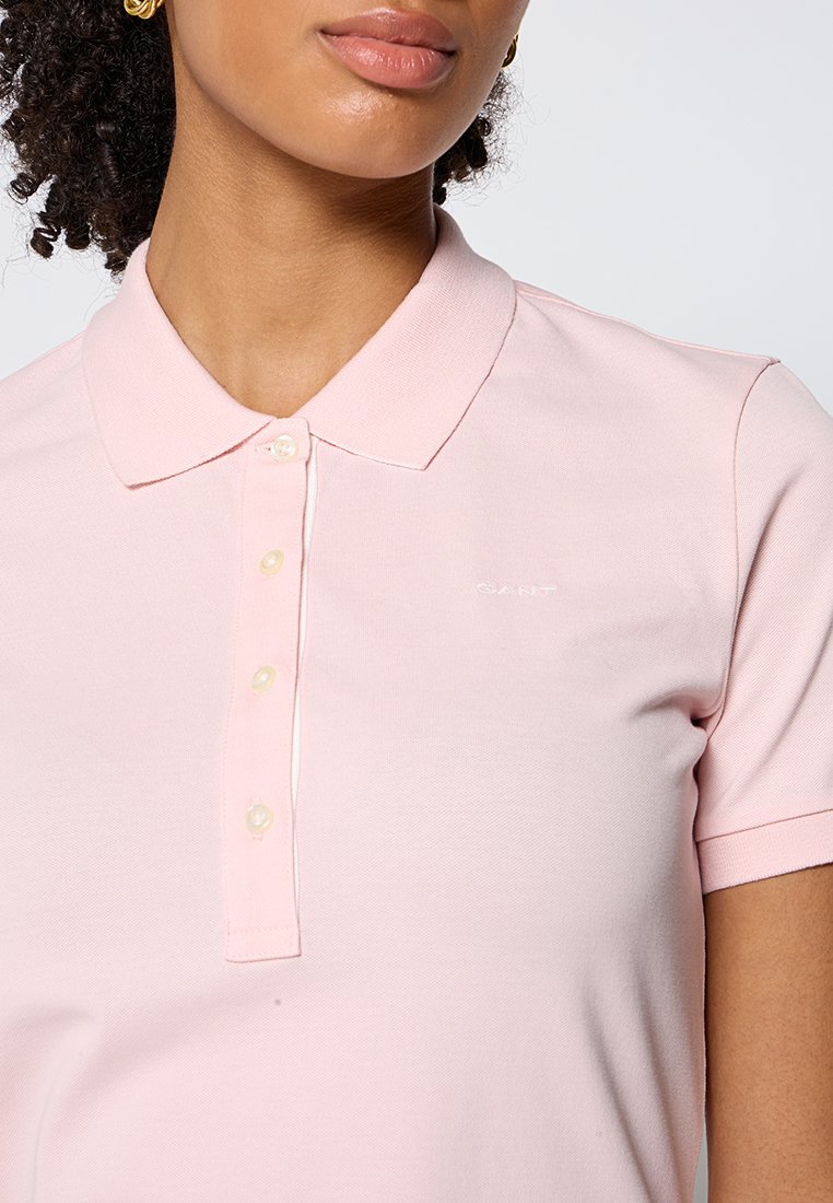 Polo shirt rose à manches courtes en tissu texturé, avec un col classique, une patte de boutonnage et une discrète marque sur la poitrine.