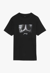 Black cotton t-shirt featuring a central graphic of hands in a praying position with the text "pray" below in a stylized white font.