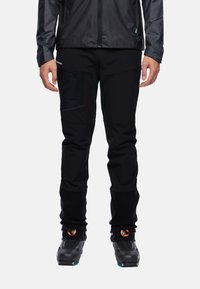 Zwarte outdoorbroeken gemaakt van ademend, flexibel materiaal. Kenmerken zijn onder andere ritszakken en een taps toelopende pasvorm bij de enkels.