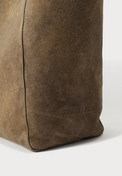 Geantă tote maro din piele întoarsă cu o textură fină, inscripționată cu marca „STAND STUDIO” în relief, formă unghiulară și detalii contrastante la cusături.