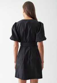 Abito nero con una vita aderente, maniche corte puffate e pieghe sul retro. Realizzato in tessuto leggero, con texture liscia.