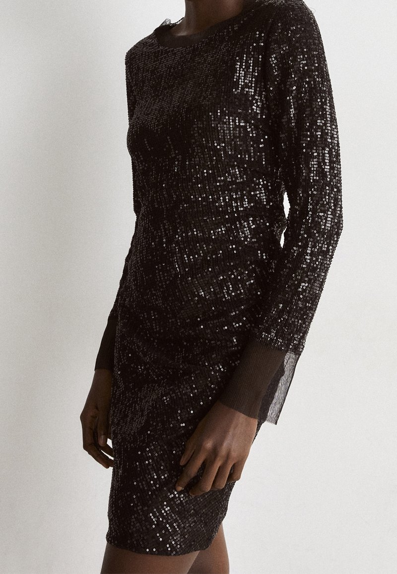 Svart paljetterad klänning med långa ärmar, figursydd design, texturerad yta och genomskinliga detaljer vid ärmsluten.