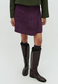 Lila tweed miniskjölt med en sidoficka och en omslagdesign, kombinerad med blanka mörkbruna knähöga stövlar med en sidogång.