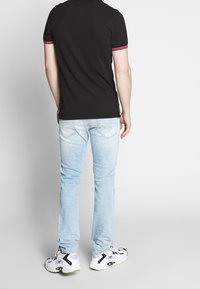 Svart polo shirt med röd och vit randig krage, ljusblå slim-fit jeans och vita sneakers med svarta och lila accenter.