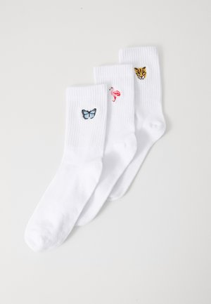 Trois paires de chaussettes blanches en coton avec des broderies colorées : un papillon bleu, un flamant rose et une tête de léopard jaune.