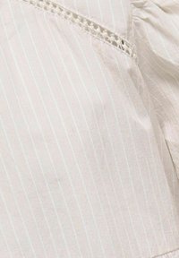 Ljust beige tyg med tunna vita ränder, med en texturerad yta och en delikat spetskant. Mjuk och luftgenomtränglig material.